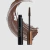 Máscara de cílios Océane Edition Tubing Mascara na cor marrom com aplicador aberto e traço de produto ao fundo