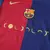 Detalhe do peito da Camisa Barcelona 2024/2025 Coldplay Home Titular I Masculino azul e bordô, com escudo centralizado e logo dourado, usada por Lewandowski, Lamine Yamal e Raphinha.