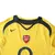 Detalhes do peito da camisa reserva Arsenal 2005/2006/2007, modelo Away II, masculina, retrô, amarela. Inclui o escudo bordado do clube, o logo da Nike em azul marinho e o patrocínio O2, representando o auge do time comandado por Arsène Wenger, com Henry,