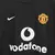 Imagem em close dos detalhes do peito da camisa reserva do Manchester United 2003/2004 preta, versão masculina, modelo Away II. Mostra o escudo bordado do clube, o logo da Nike em branco e o patrocínio Vodafone em destaque, uma peça icônica vestida por Cr