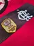 Detalhes do peito da camisa titular do Flamengo 2023/2024, mostrando o escudo do clube em destaque, o logo da Adidas em branco e o monograma “CRF”, com design rubro-negro em modelo masculino, representando Gabigol e Pedro Arrascaeta.