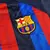 Escudo do Barcelona na camisa titular 2022/2023 Home masculina, aplicado no peito esquerdo. O escudo é acompanhado do logo Nike Swoosh dourado e do patrocínio Spotify em dourado. O design da camisa celebra a transformação da cidade com listras verticais e