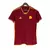 Frente da camisa titular home da Roma 2023/2024, predominantemente vermelha com detalhes em amarelo, incluindo as três listras da Adidas nos ombros e o escudo histórico com o Lupetto, representando a rica tradição do clube. Destaque para os jogadores Dyba