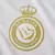 Escudo do Al-Nassr na terceira camisa 2024/2025, modelo masculino, nas cores branca e dourada. Usada por Cristiano Ronaldo (CR7), Anderson Talisca e Sadio Mané, a camisa traz o escudo em destaque no peito esquerdo, com o logo da Adidas dourado no lado dir