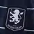 Escudo do Aston Villa na terceira camisa 2024/2025 III Third Masculino azul marinho, em fundo preto com leão e nome do clube em prateado. Escudo posicionado no lado esquerdo do peito, complementando os detalhes em prata no restante da camisa.