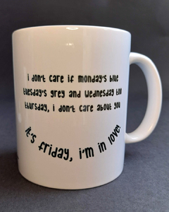 caneca branca com desenho de uma criança sorridente, de cabelos enrolados, com a frase " I don't care if Monday's blue/ Tuesday's grey and Wednesday too/ Thursday, I don't care about you/ It's Friday, I'm in love"