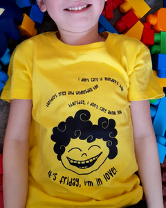 camiseta amarela com desenho de uma criança sorridente, de cabelos enrolados, com a frase " I don't care if Monday's blue/ Tuesday's grey and Wednesday too/ Thursday, I don't care about you/ It's Friday, I'm in love", em tamanho infantil, sem gênero