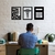 Um homem sentado em uma mesa de escritório, olhando para a tela do computador, com três quadros decorativos na parede sobre contabilidade, um símbolo de saúde e uma calculadora.