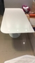 Mesa branca moderna com base circular, refletindo luz em um ambiente interno.