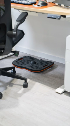 Tapete antifadiga Board posicionado sob uma mesa com regulagem de altura, ao lado de uma cadeira ergonômica.