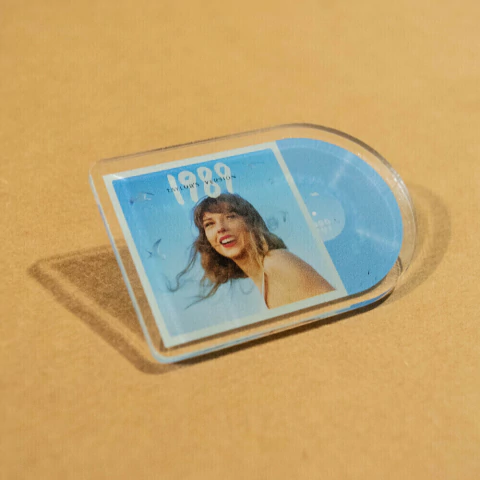 Pin de colección de Taylor Swift con diseño del álbum 1989, mostrando una imagen de la artista y un fondo azul.