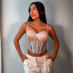 Corset Victoria de encaje celeste con tirantes finos, combinado con pantalones blancos, modelado por mujer con cabello largo y suelto.