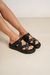 Sandalias bajas negras de la colección Primavera-Verano 2025, con detalles metálicos y diseño cruzado.