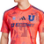 Camiseta naranja de la Universidad de Chile para hombres, modelo visitante 2025 de Adidas, con logotipos y diseño moderno.