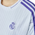 Camiseta blanca de hombre del Real Madrid con el escudo del club en el pecho y detalles en morado.