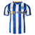 Camiseta FC Porto Home 24/25: Vista frontal. Rayas azules y blancas estilizadas con gráfico de humo. Cuello azul y blanco. Escudo del FC Porto en el pecho izquierdo, logo de New Balance en el pecho derecho.