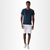 Camiseta masculina na cor marinho, com tecido de malha fria, usada por um modelo em pé, com shorts cinza e tênis claro.