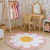 Tapete infantil redondo com estampa de flor rosa e centro amarelo em quarto decorado com móveis de madeira clara e vestidos coloridos pendurados