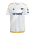  "Camisa titular do LA Galaxy, temporada 2024, cor branca com finas linhas azul marinho e detalhes em amarelo, vista frontal."
