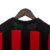 Vista traseira da camisa do Milan 2003, com listras vermelhas e pretas, pendurada em um cabide.