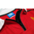 Detalhe da camisa vermelha do Manchester United de 1998, mostrando o logo da Umbro e o fechamento com zíper.