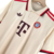 Detalhe da Gola Polo Bege com Frisos Vermelhos e Bordô e Patrocínio Deutsche Telekom na Camisa 3 Bayern 24/25