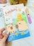 Caderno A5 com ilustração de capivaras fofas na floresta, segurando frutas e brincando na água.