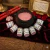 Kit com 7 pós de mironga para rituais de aproximação e conquista do amor da marca 7 Folhas, dispostos em semicírculo ao redor de um caldeirão com pó rosa, decorado com velas vermelhas e pétalas de rosa.