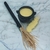 Pó de Mironga Chama Dinheiro 5g da 7 Folhas com mini caldeirão e vassoura de bruxa sobre elegante base de mármore. Utilize em rituais para melhorar a entrada de dinheiro e sorte nos jogos.