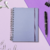 Caderno Smart médio com folhas reposicionáveis em fundo azul bebê, ao lado de caneta, clipes e fones de ouvido.