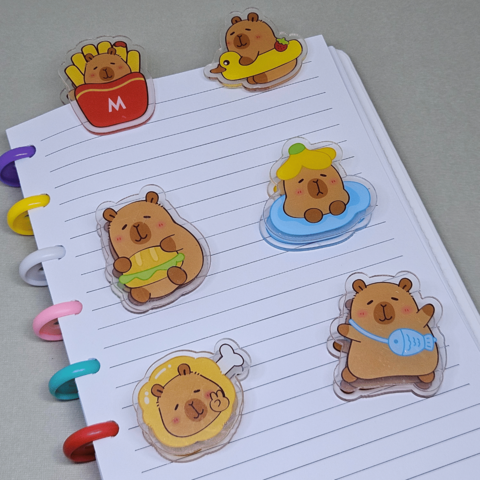 Kit com 6 prendedores de acrílico com desenhos de capivaras em várias atividades divertidas, como comendo e brincando.