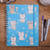 Caderno A5 com estampa de gatinhos em fundo azul, acompanhado de canetas sobre uma mesa de madeira.