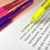 Marca texto gel retrátil da Tris, destacando texto em uma folha, com outras canetas coloridas ao fundo.