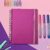 Caderno Smart com capa pink e espiral, ao lado de canetas coloridas e clipes de papel.