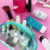 Estojo DAC com zíper Trator Collab Bubble e Breeze com produtos de beleza e maquiagem dentro, em um fundo rosa.