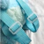 Detalhe das alças ajustáveis da mochila de pelúcia Lilo & Stitch, destacando a cor azul e os fechos plásticos.