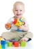 Criança sorridente segurando um brinquedo furadeira colorido e um bloco laranja, com cubos de brinquedo ao redor.