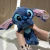Boneco de pelúcia azul com orelhas rosa, segurado por uma mão, com olhos grandes e expressivos.