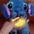 Ursinho pelúcia do Lilo and Stitch, com luz suave no peito e movimento de respiração, sendo acariciado por uma mão.