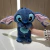 Boneco de pelúcia azul, inspirado no personagem Stitch, com grandes orelhas rosa e expressão fofa, segurado por uma mão.