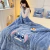 Mulher sentada em uma cama coberta com um edredom azul com estampa do personagem Stitch, da Disney. Ela está segurando o edredom em um ambiente aconchegante.