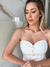 Mulher com vestido branco sem alças, usando colar dourado, posando em ambiente iluminado.
