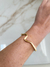 Pulseira dourada com design sinuoso, ajustada no pulso de uma mão.