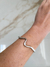 Pulseira prateada com design ondulado, vista no pulso de uma mão.
