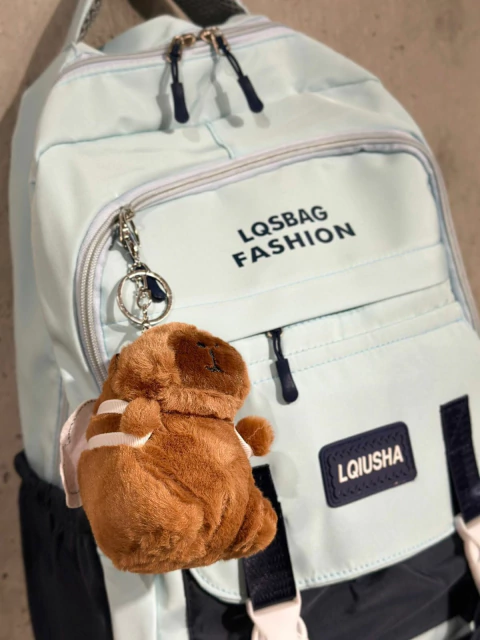 Mochila escolar urbana combinada en tonos claros con colgante de peluche capibara y bolsillo frontal con cierre