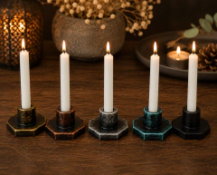 Candelabros compactos artesanales de diferentes colores con velas blancas encendidas sobre mesa de madera.