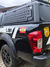 Capota Torden Adventure instalada em uma Nissan Frontier 2024, com detalhes da parte traseira do veículo,torna visivel as grades laterais fixadas nas portas da capota e adesivos da polícia civil, provando da qualidade e responsabilidade com os produtos.