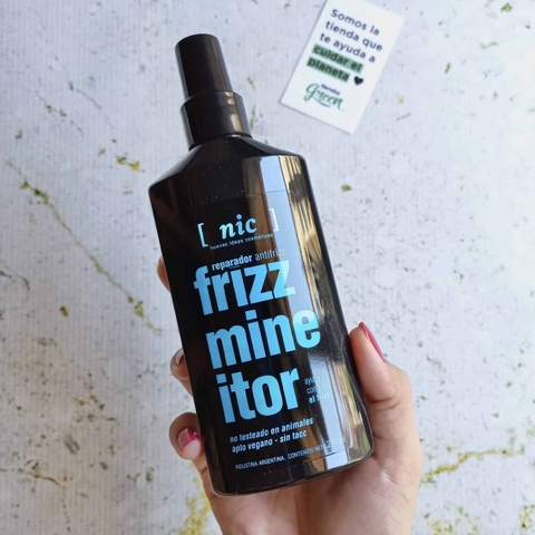 Botella del tratamiento reparador antifrizz Frizzmineitor de NIC, presentada en una mano. El envase es negro con texto azul que describe el producto.