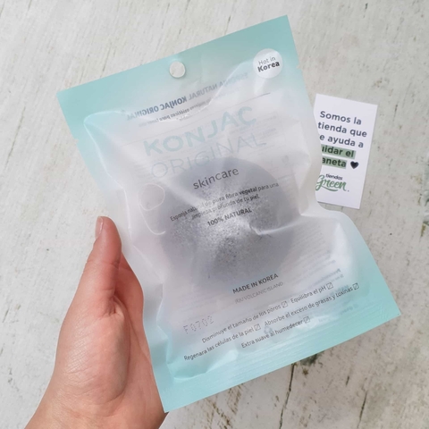 Esponja Konjac facial negra con carbón en su empaque, sostenida por una mano.
