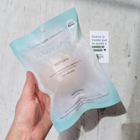 Esponja facial blanca 100% Konjac en su empaque, sostenida con una mano, ideal para todo tipo de piel.